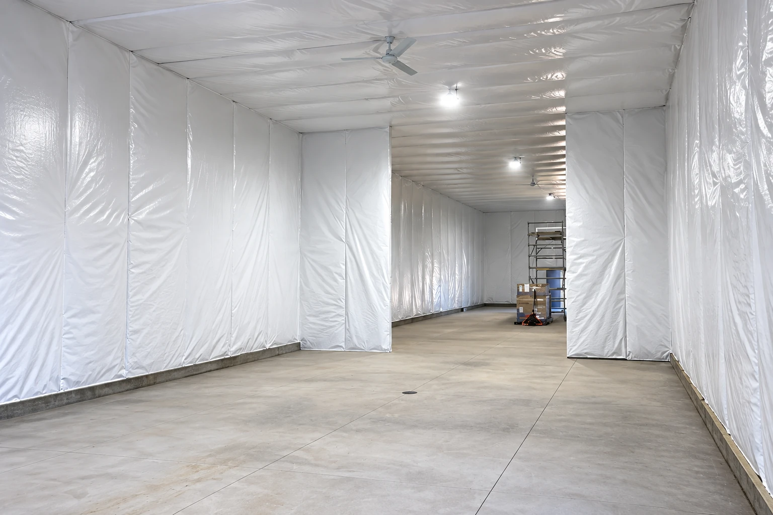 A large commercial interior is lined with white plastic sheeting on its walls and ceiling, with a concrete floor.
