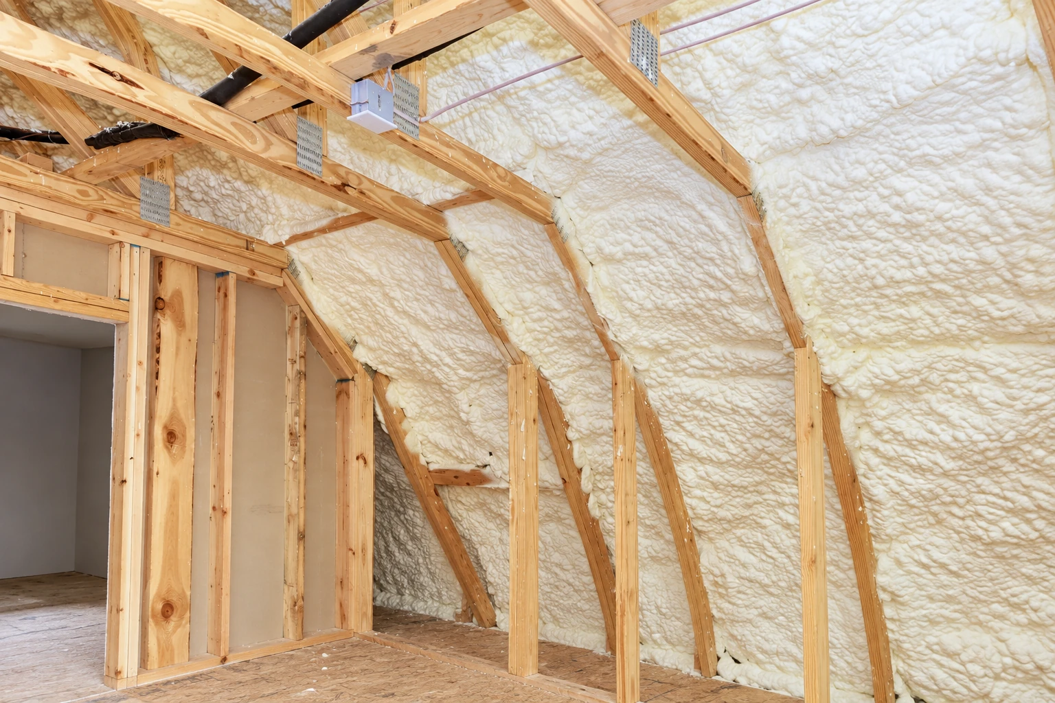 Spray foam insulation fills the roof and wall cavities of a partially framed room.