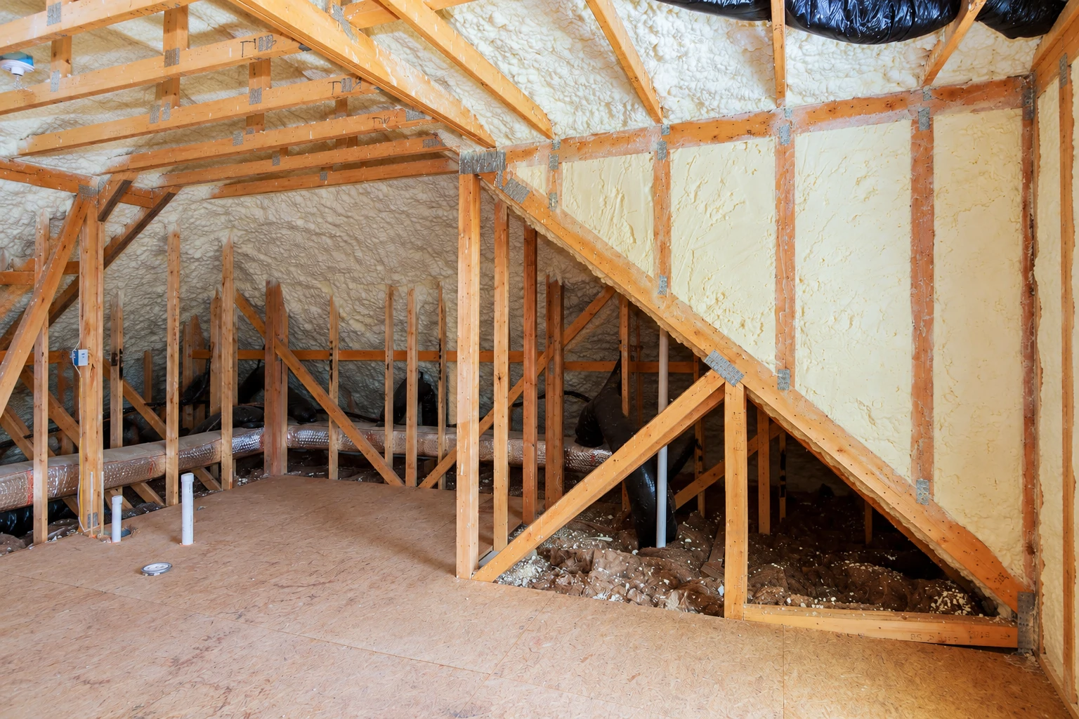 Spray foam insulation coats the sloped attic roof and walls around exposed wooden trusses.